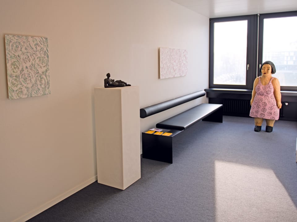 Bemalte Holzfigur von Alois Hermann vor einem Fenster.