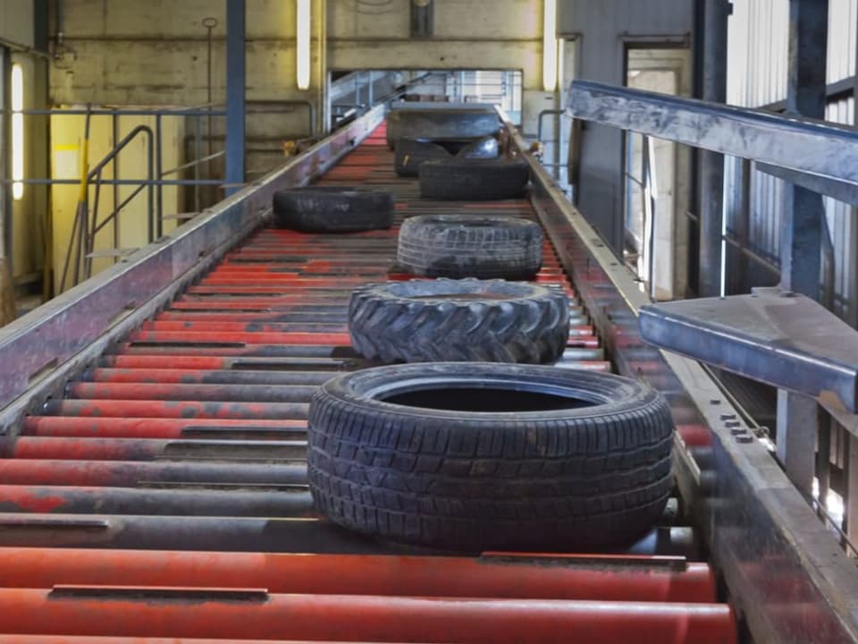 Alte Autoreifen werden auf einer rotem Laufband bewegt. 