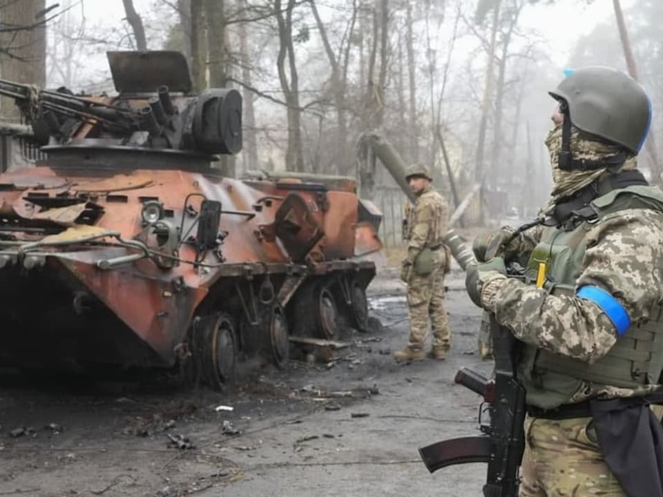 Ukrainische Soldaten stehen neben einem zerstörten Panzer.