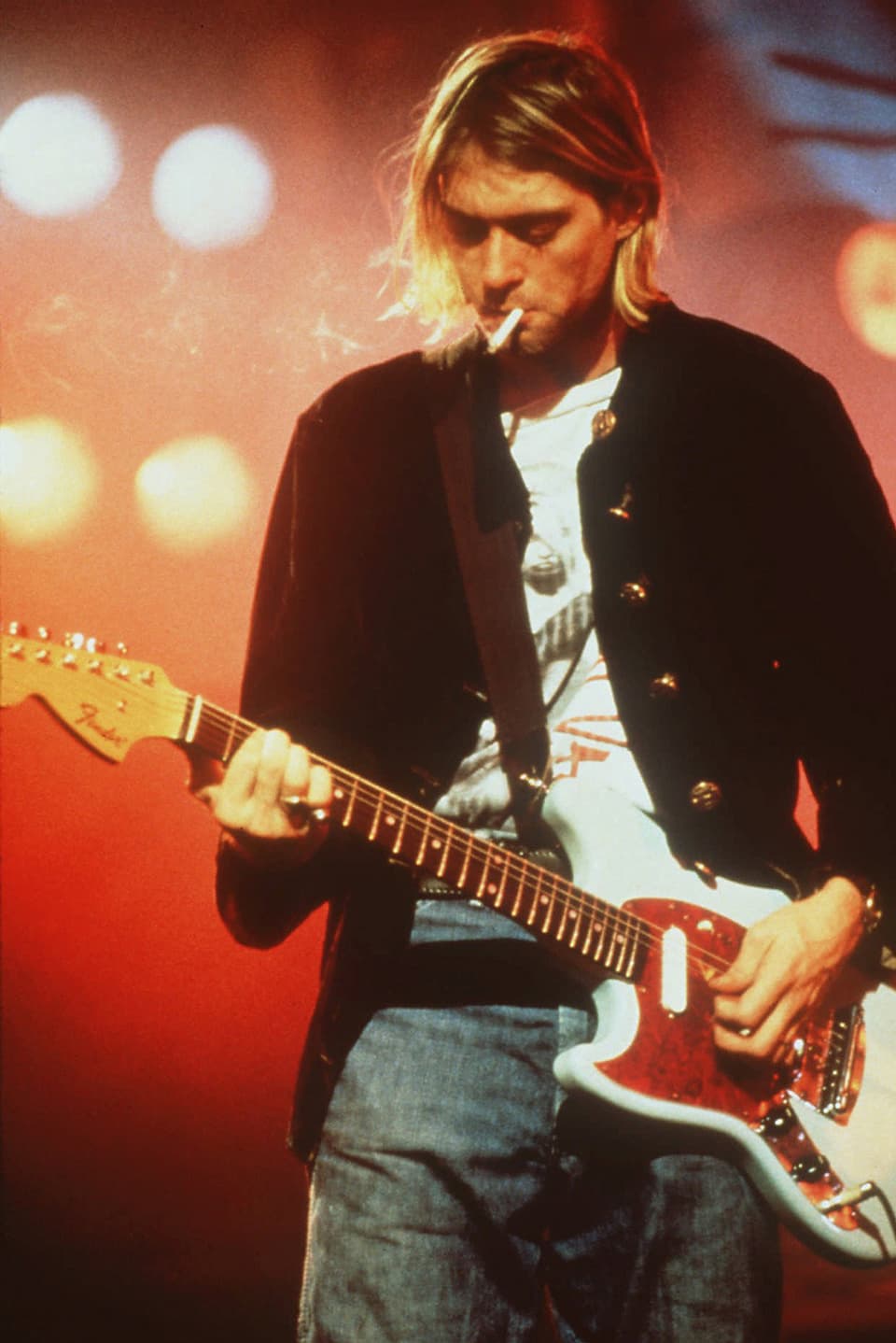 Zu sehen ist der Frontman der Grungeband Nirvana, Kurt Cobain. Er spielt Gitarre und hat eine Zigarette im Mund.