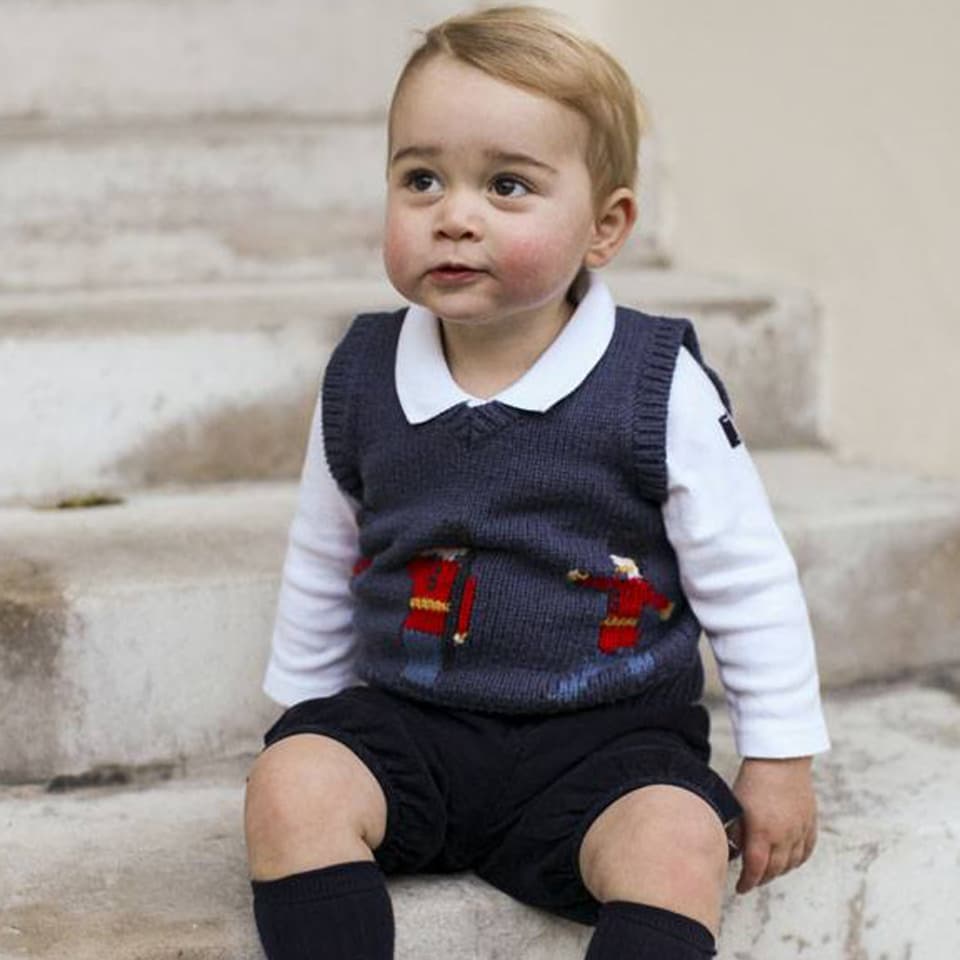 Baby George in kurzen Hosen auf einer Steintreppe sitzend.