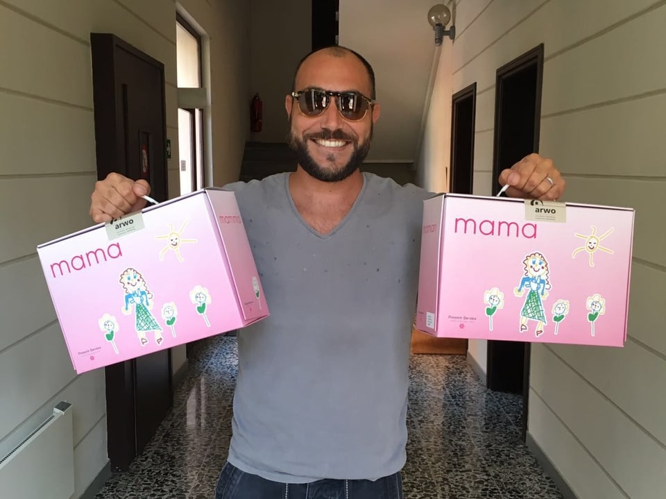 Giovanni Marchese hält zwei pinke Boxen in der Hand und hält sie lächelnd in die Kamera.