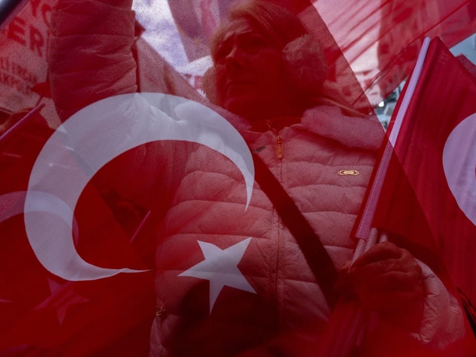 Mehrere türkische Flaggen werden geschwenkt; dahinter eine Frau