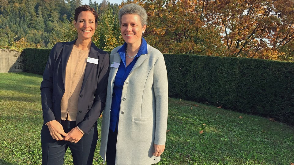 Zwei Frauen stehen nebeneinander auf einer Wiese. 