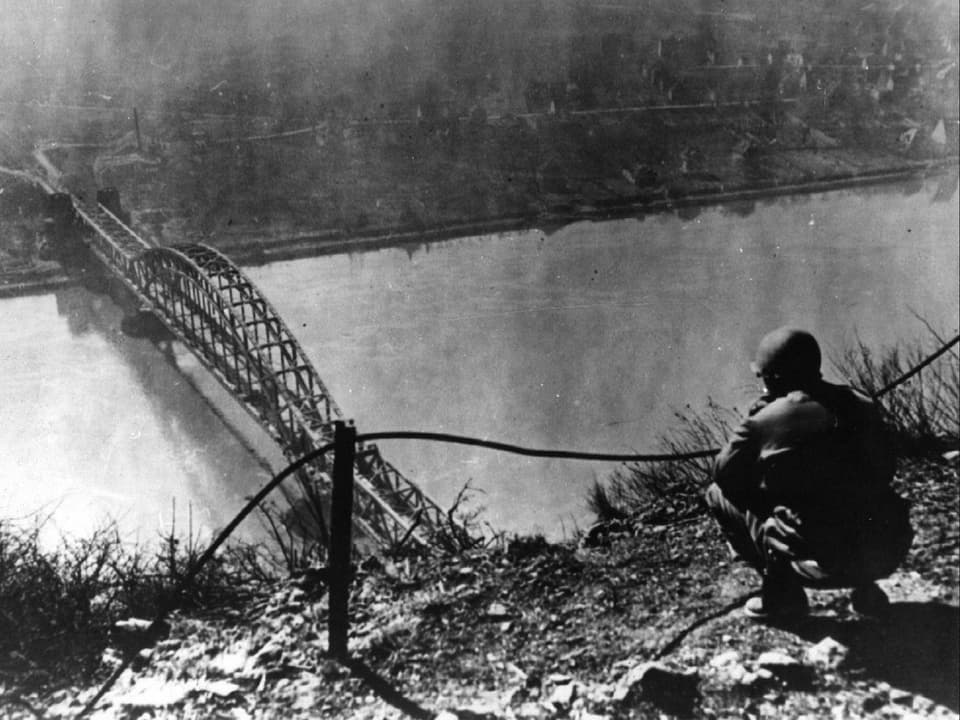 Das Schwarzweiss-Foto zeigt einen US-Soldaten, der die Brücke von Remagen von einem Hügel aus observiert.