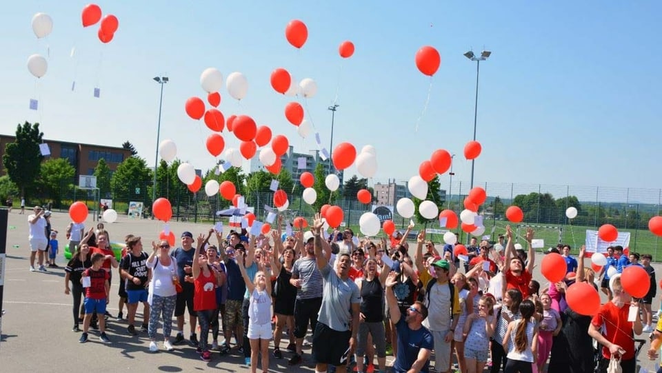 Menschen in Turnklamotten lassen Ballone steigen und feiern, im Hintergrund Wohnblöcke