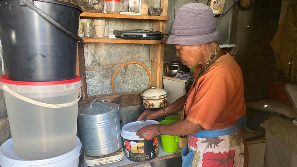 Eine ältere Frau werkelt in einer behelfsmässigen Küche.