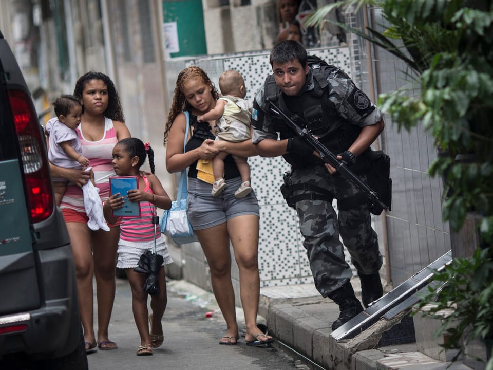 Frauen mit Kindern werden von einem Militärpolizisten begleitet.