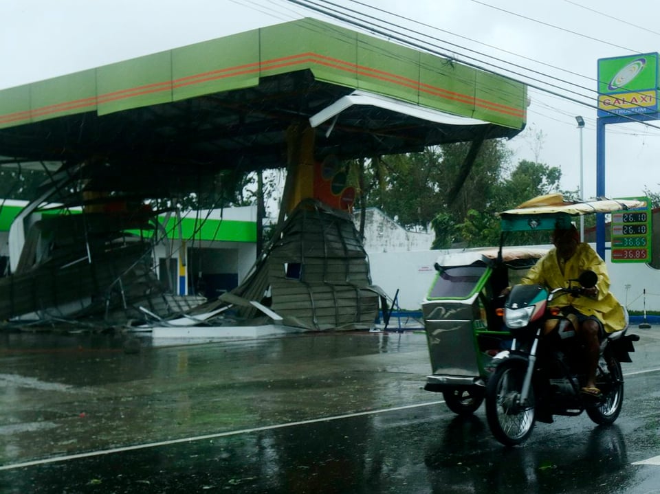 Motorrad fährt an einer Tankstelle mit beschädigtem Dach vorbei