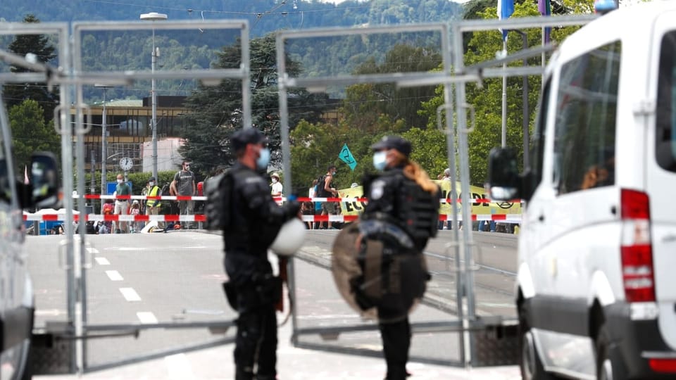 Polizist und Polizistin hinter Metallgerüst, in der Ferne Demonstranten