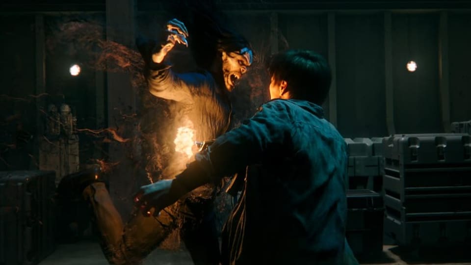 Mann über Feuer, schwingt riesige Klaue, Gesicht zur Fratze verzerrt. Neben ihm junger Mann mit dem Rücken zum Foto.