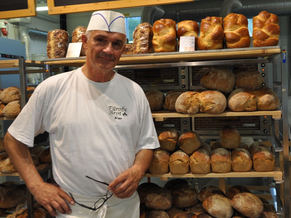 Ein Mann in weisser Kleidung steht vor einem Gestell mit Brot.