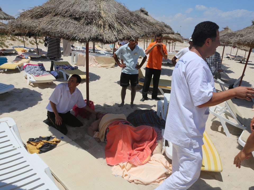 Rettungskräfte versorgen den einen Verletzten am Strand unter einem Schilfsonnenschirm.