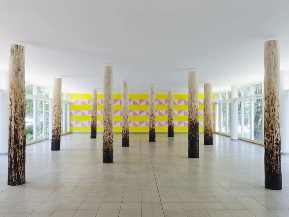 Ausstellung von Claudia Comte: halb angeschwärzte Baumstämme vor einer Wandgrafik.