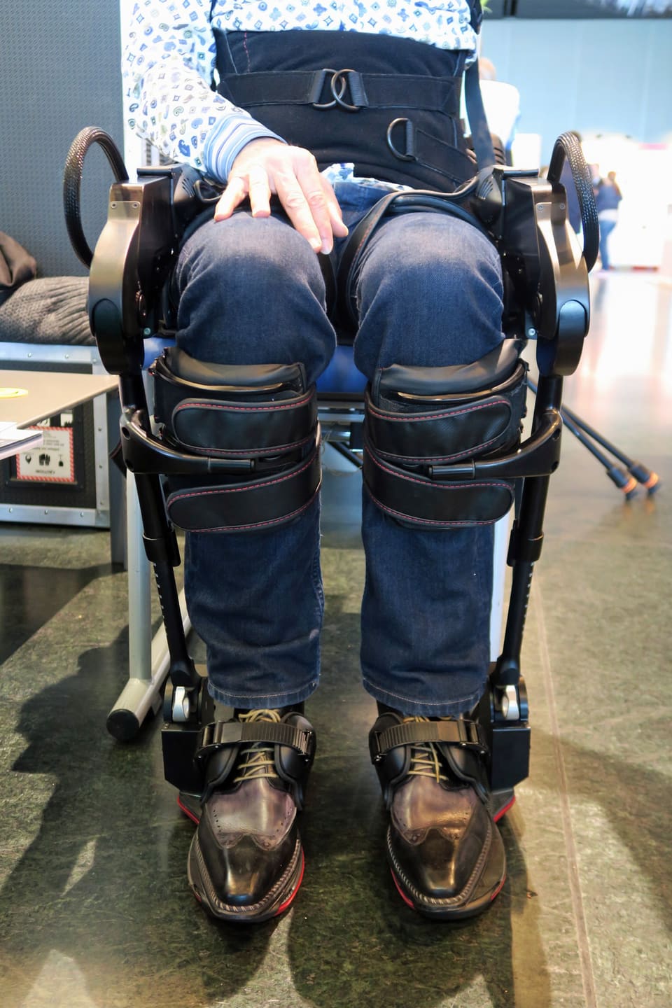 Die Beine eines Rollstuhlfahrers an einem Laufroboter.