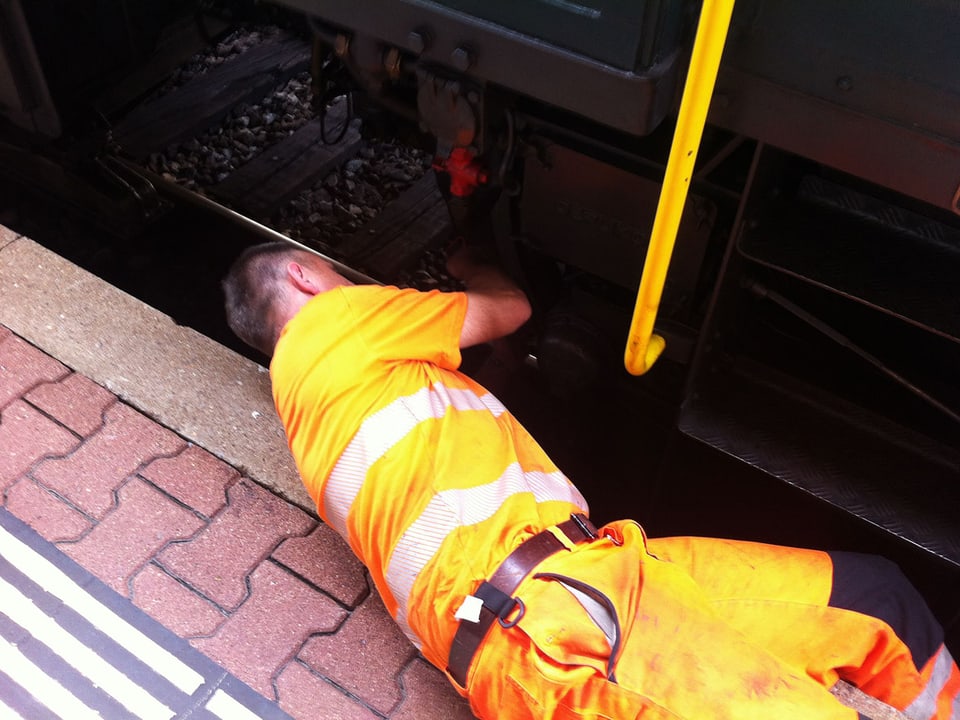 Ein Mann in oranger Uniform ist an der Lokomotive am Werk.