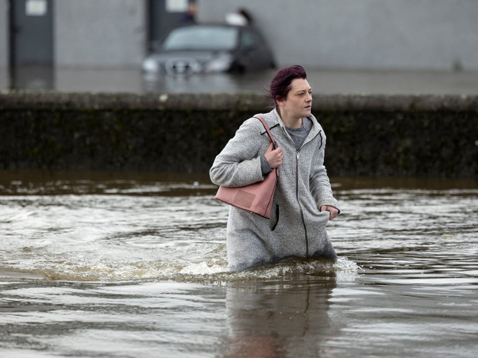 Eine Frau schreitet durch Wassermassen nach heftigen Regenfellen im Zuge des Sturmtiefs in Nordirland. 