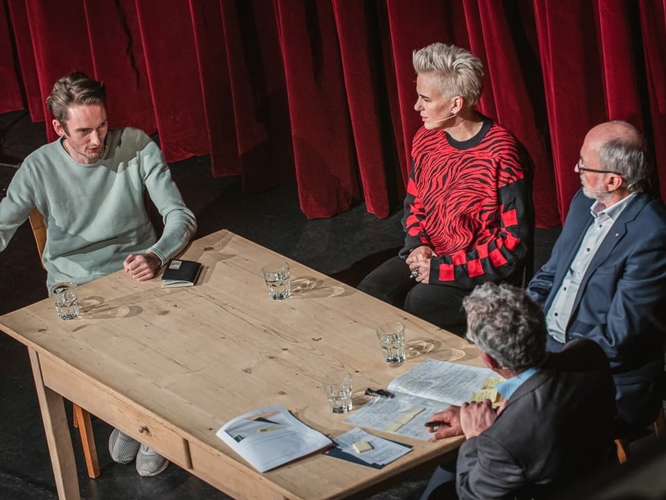 Drei Unternehmer sitzen an einem Tisch und diskutieren mit dem Moderator