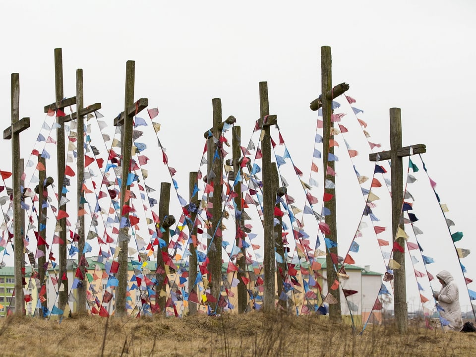 Hölzerne Kreuze mit farbigen Flaggen auf einem Hügel.