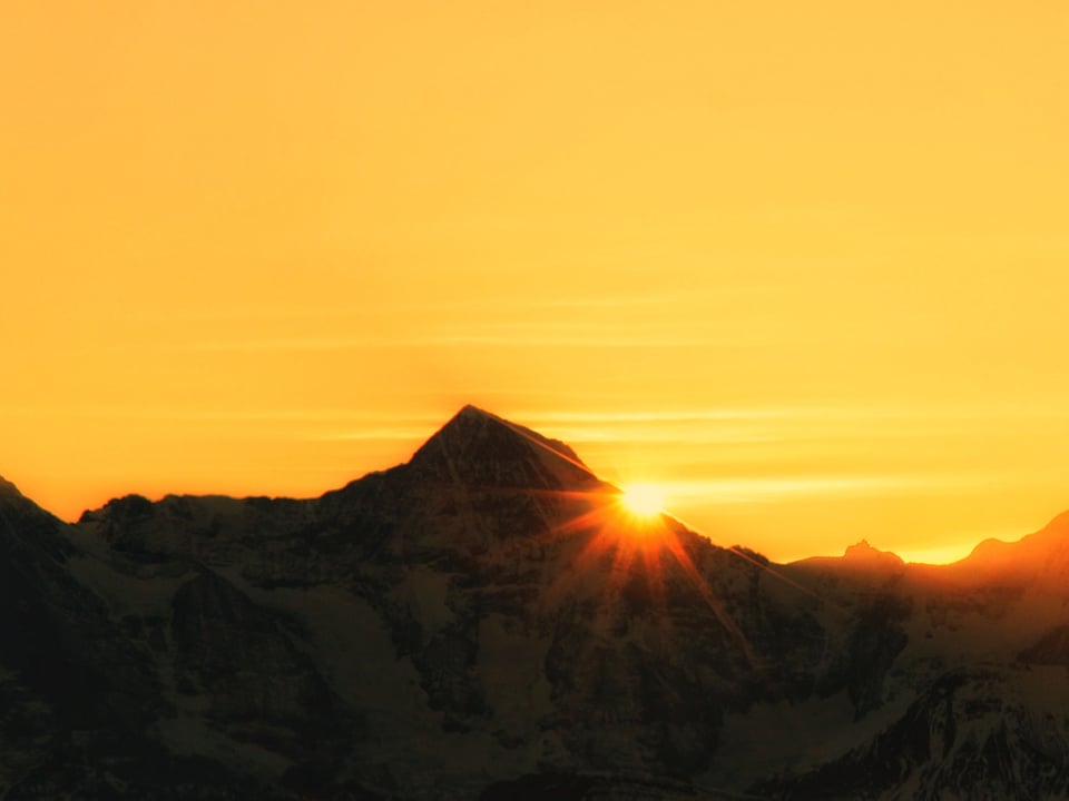 Sonnenaufgang direkt beim Bergkamm. Dahinter gelblicher Himmel.