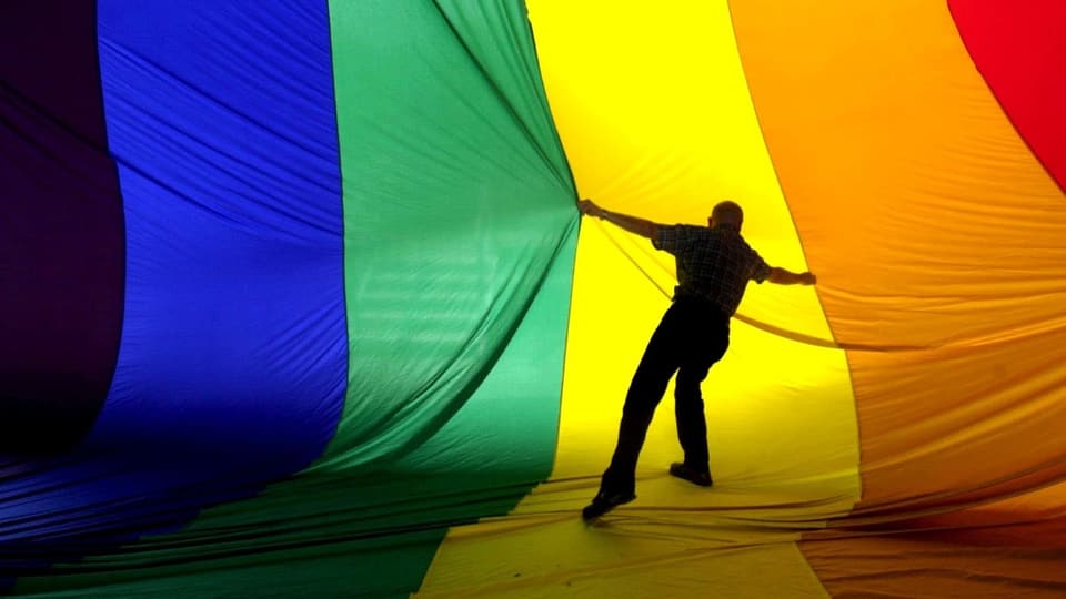 Person ist vor einer sehr grossen Regenbogenflagge und zieht daran.
