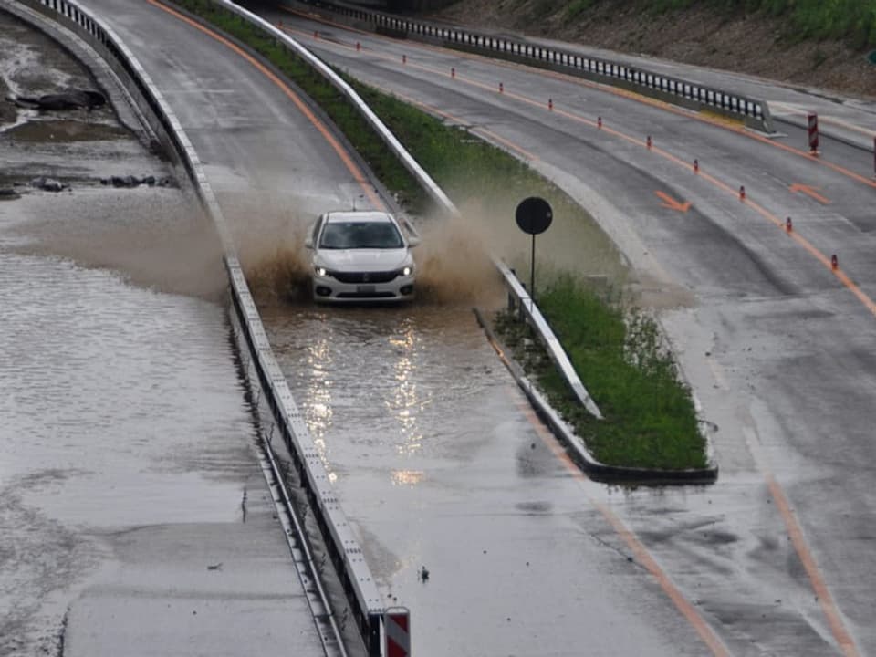 Überflutete Autobahn mit viel Wasser auf der Fahrbahn und einem Auto