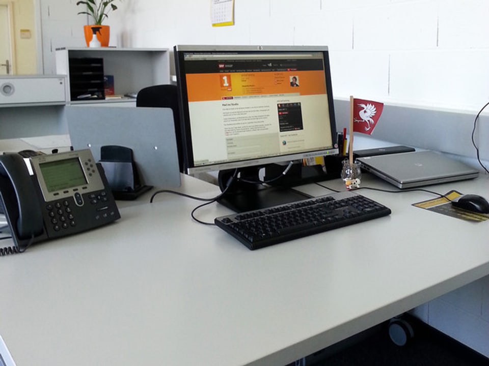 Aufgeräumter Schreibtisch mit Bildschirm, auf der die Webseite von SRF zu sehen ist.