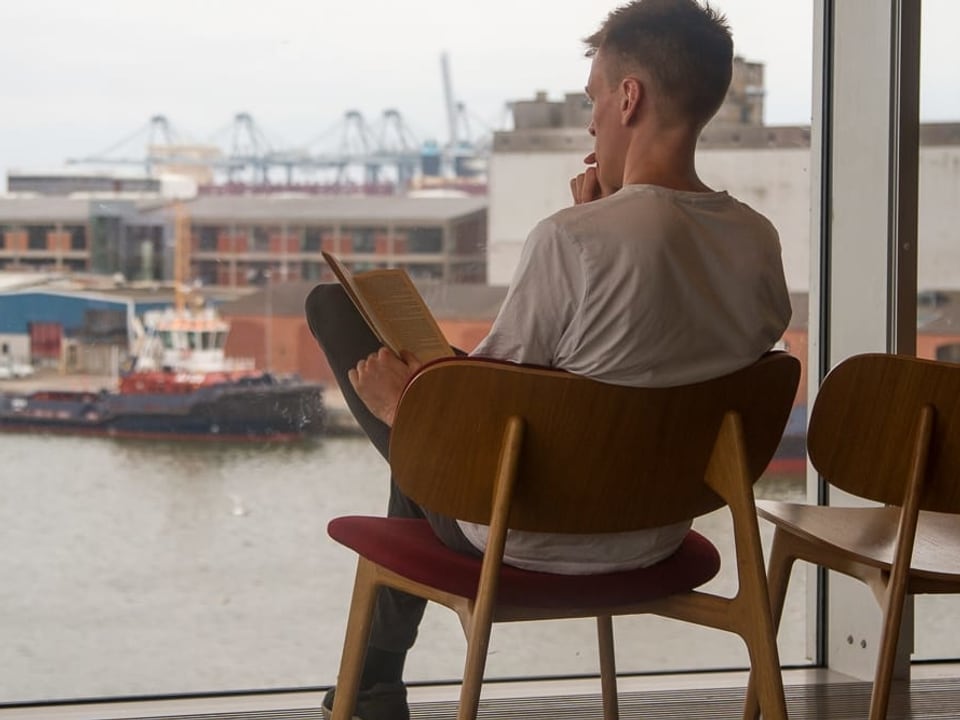 Ein junger Mann liest ein Buch mit Blick auf einen Hafen.