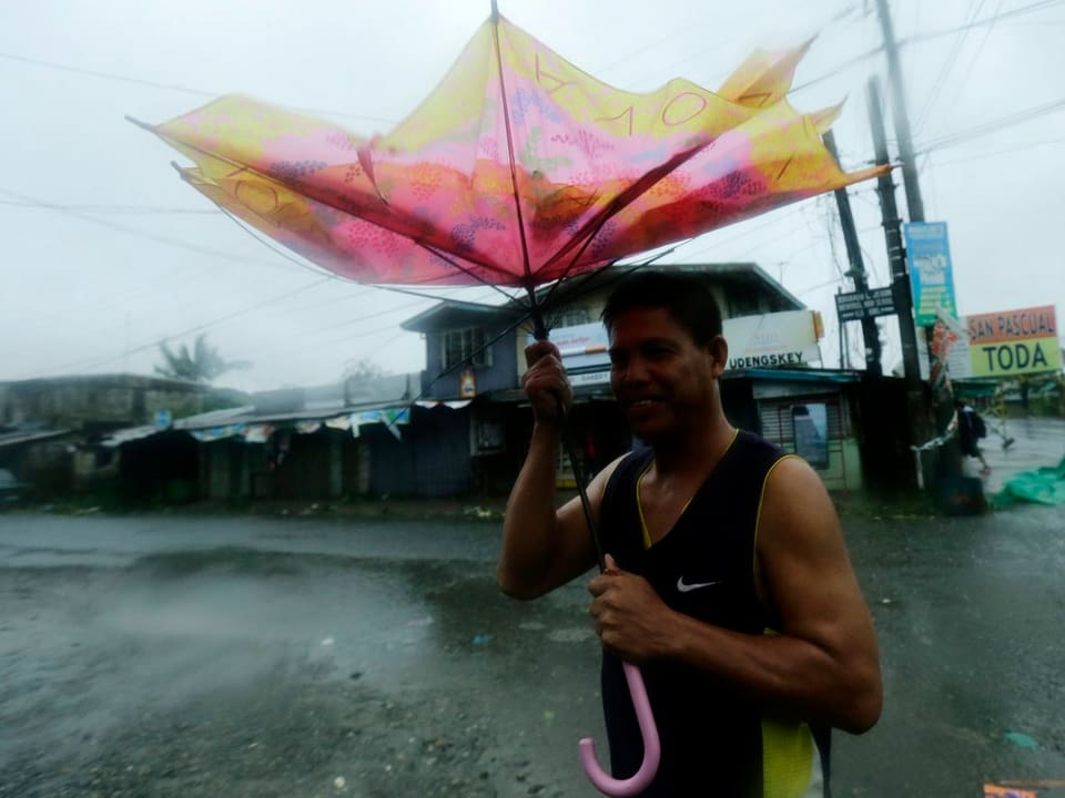 Mann hält einen zerzaustem rosa-gelben Regenschirm über sich