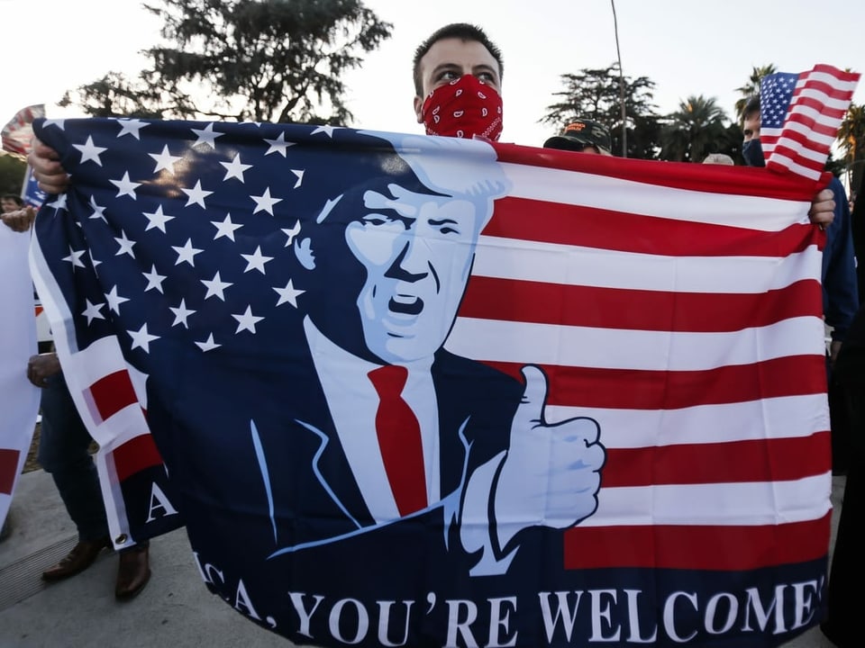 Ein Trumpanhänger hält eine Fahne mit Trumps Gesicht hoch.