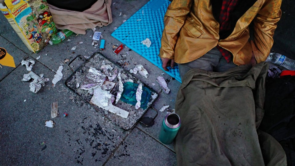 Ein Drogenabhängiger sitzt am Boden, daneben Utensilien, die er für den Drogenkonsum benötigte.