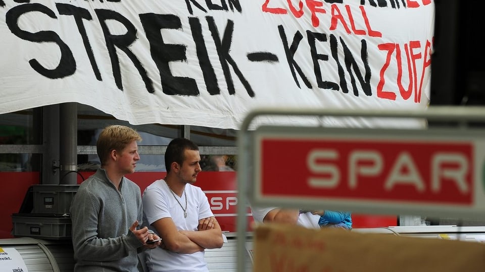 Zwei Personen stehen unter dem Streikbanner der Mitarbeiter, bei der Spar-Tankstelle in Baden-Dättwil.