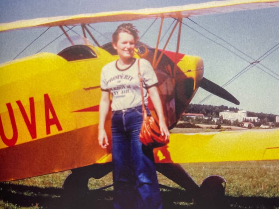 Fotografie einer jungen Frau, die vor einem Flugzeug steht.