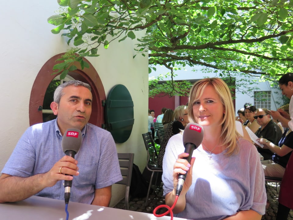 Atici sitzt links und Milanovic rechts in einem Gartenrestaurant. Sie halten SRF-Mikrofone in der Hand.