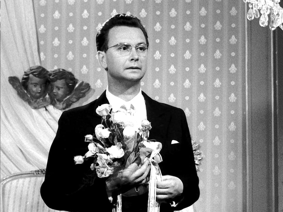 Ein Mann mit Brille hält einen Strauss weisser Rose in der Hand.
