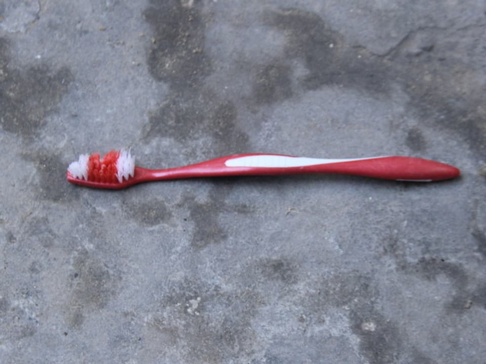 Eine rot-weisse, abgenutzte Plastikzahnbürste liegt auf grauem Asphalt