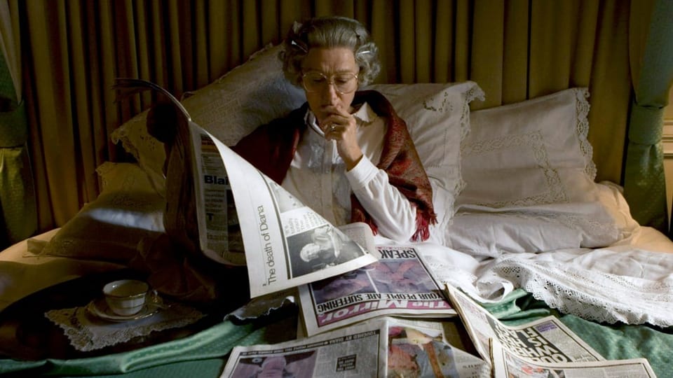 Frau mit grauen Haaren und Brille sitzt im Bett, liest Zeitung, viele Zeitungen darum herum auf dem Bett.