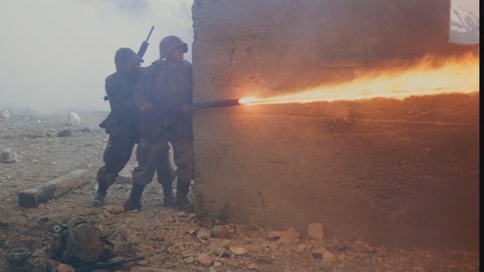 Zwei Soldaten verstecken sich hinter einer Mauer und feuern aus einem Flammenwerfer um die Ecke.