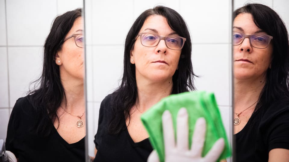 Eine Frau wird dreifach beim reinigen eines Badezimmerspiegels gespiegelt.