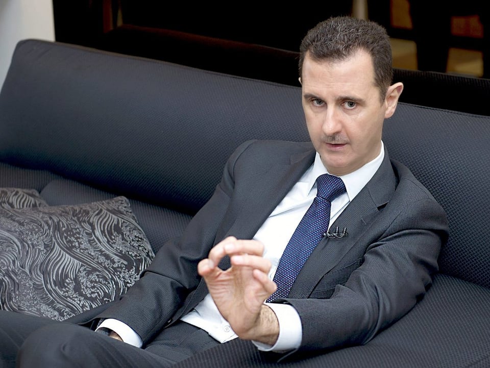 Syriens Präsident Bashar al-Assad sitzt auf einem grauen Sofa.