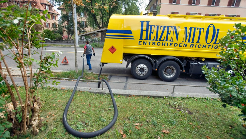 Symbolbild: Ein gelber Heizöl-Tankwagen steht am Strassenrand, der Einfüllschlauch auf einer Wiese ausgebreitet.