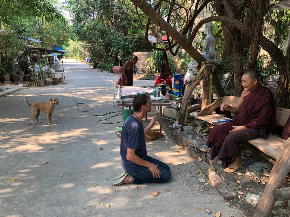 Eine Person kniet vor einem Mönch in einer Parkanlage.