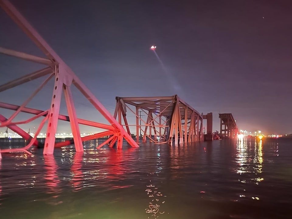 Rot schimmernde Brückenteile im Wasser bei Nacht.