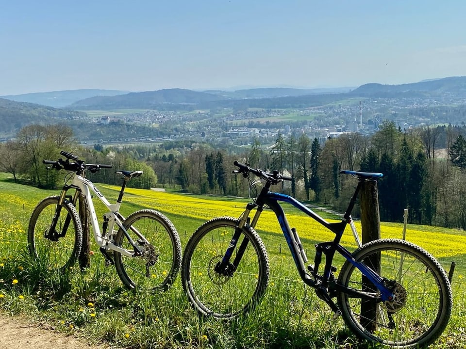 Zwei Mountainbikes vor einer Wiese mit Hügeln im Hintergrund