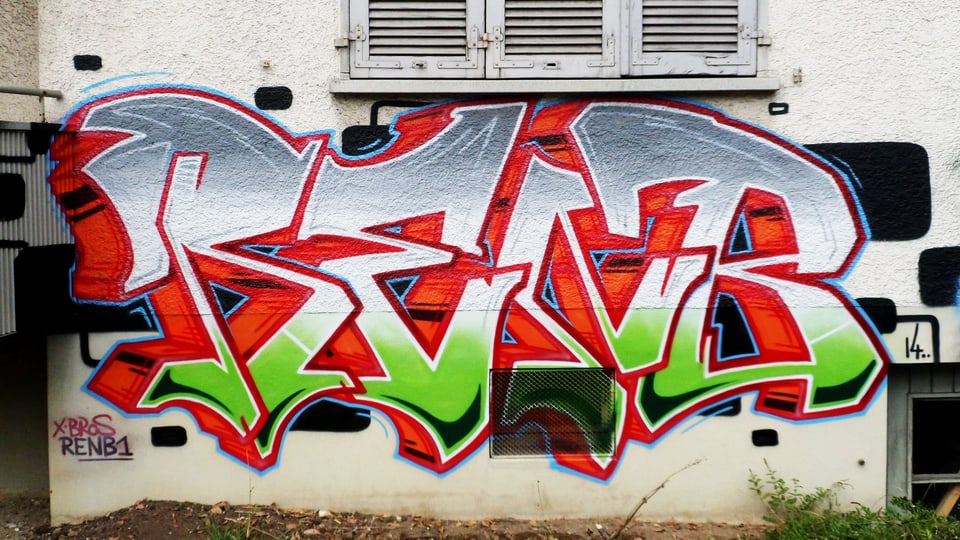 Graffito in Grün, Grau und Rot auf eine Hauswand gesprayt.