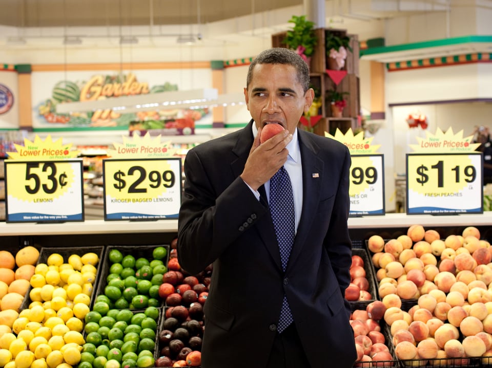 Barack Obama steht in einem Supermarkt und beisst in eine Nektarine.