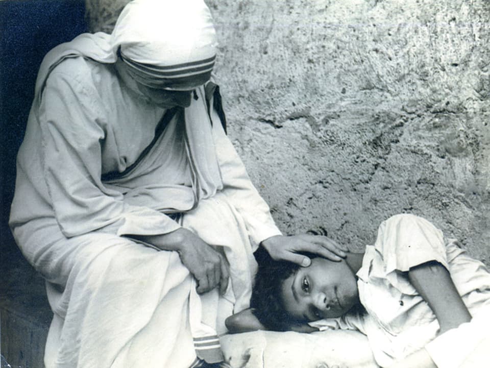 Mutter Teresa streichelt einem liegenden Kind über die Wange