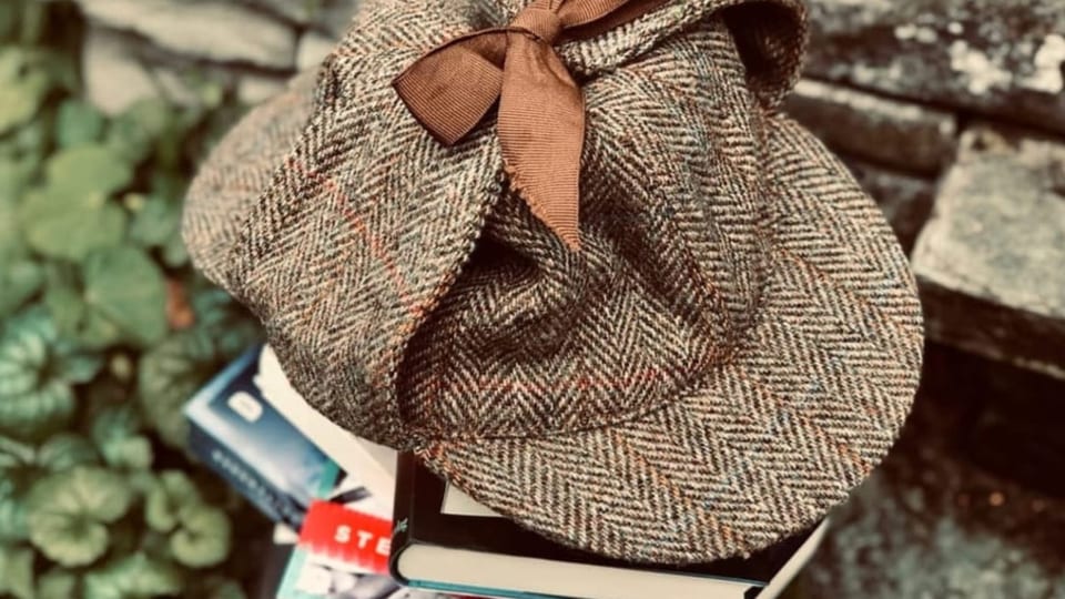 Auf einem Bücherstapel liegt eine Sherlock Holmes Kappe