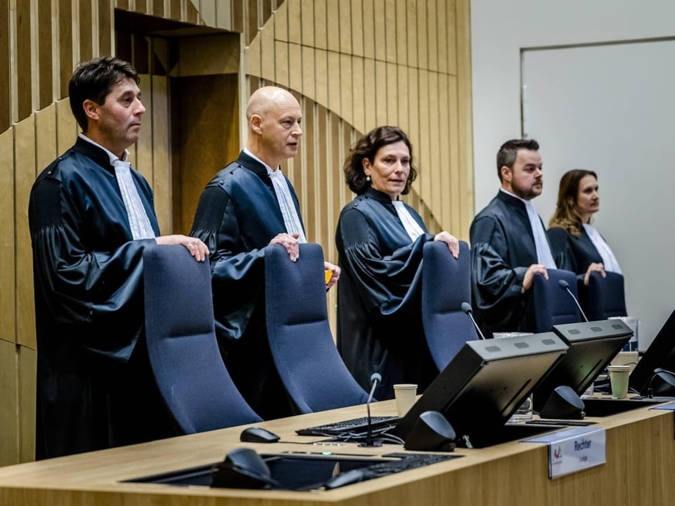 Drei Richter und zwei Richterinnen stehen nebeneinander hinter ihren Stühlen im Gerichtssaal.