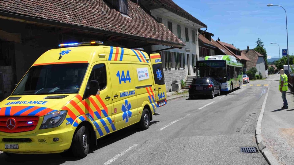 Ambulanz am Strassenrand, dahinter Unfall mit Auto und Bus 